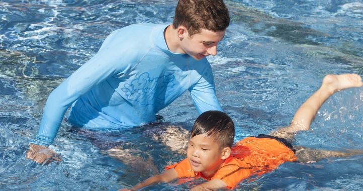 Boy in orange rash vest learning to swim with a kickboard